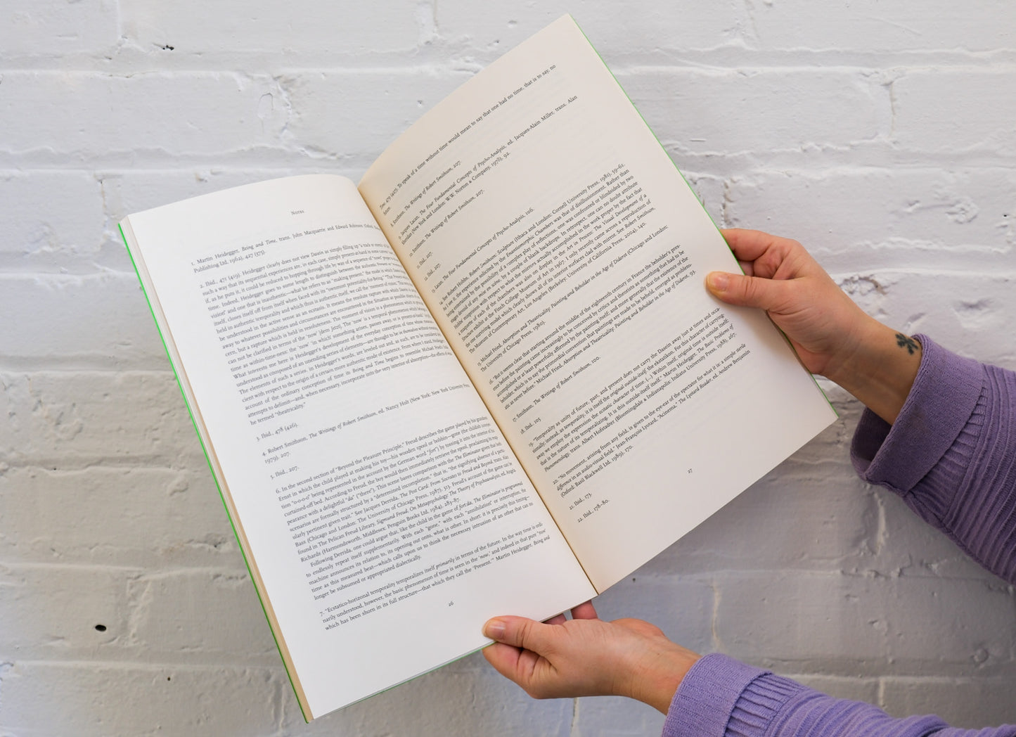Person holding an open book against a white brick wall
