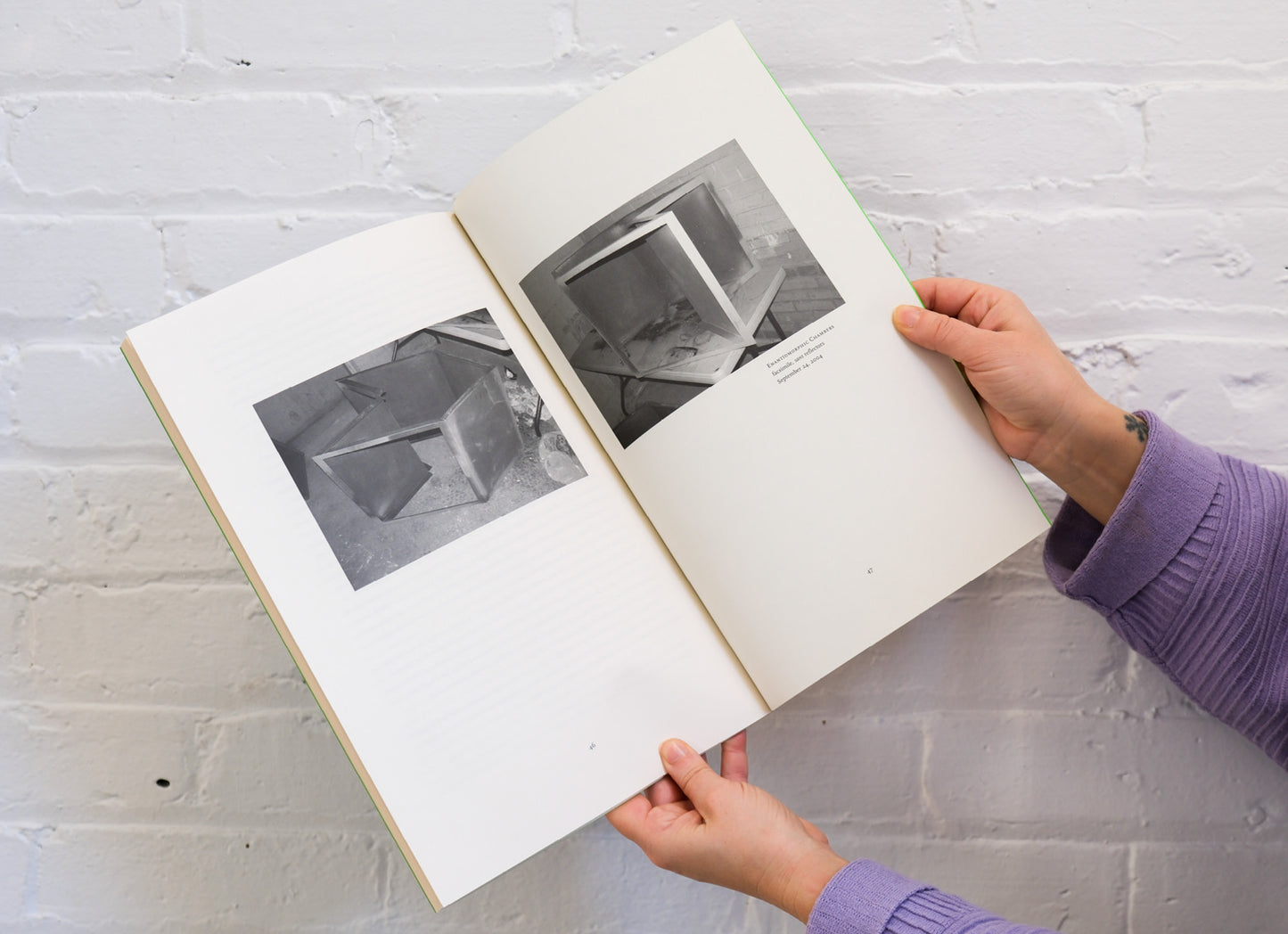 Person holding an open book with black and white photographs on a light gray surface.