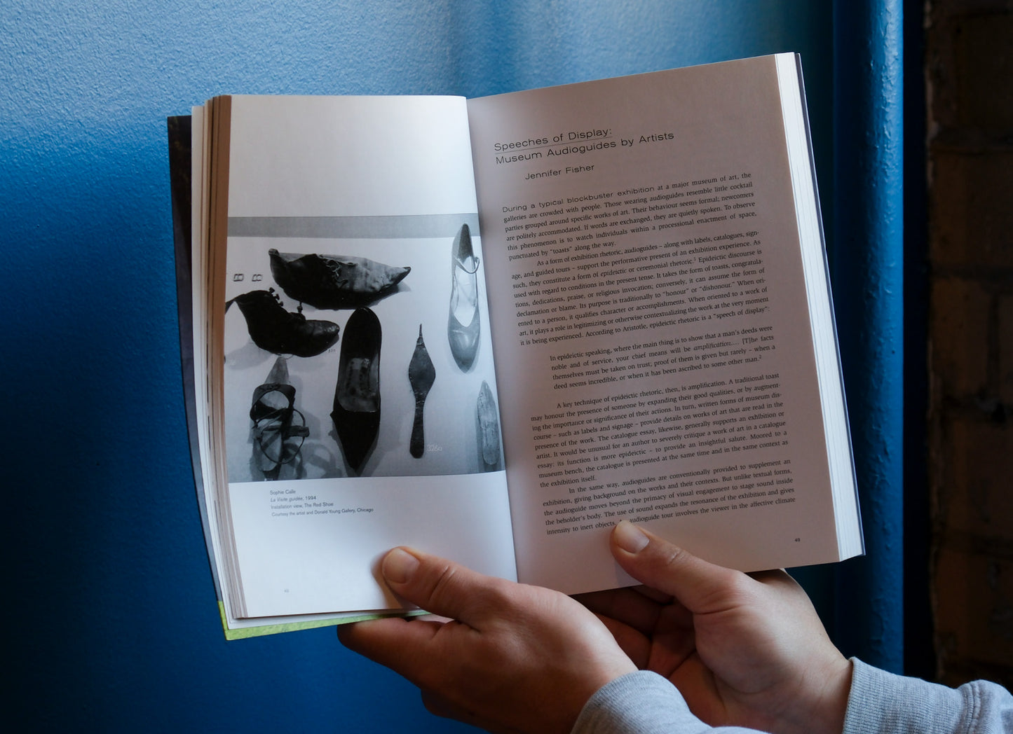 Open book with black and white images and text held by a person against a blue background