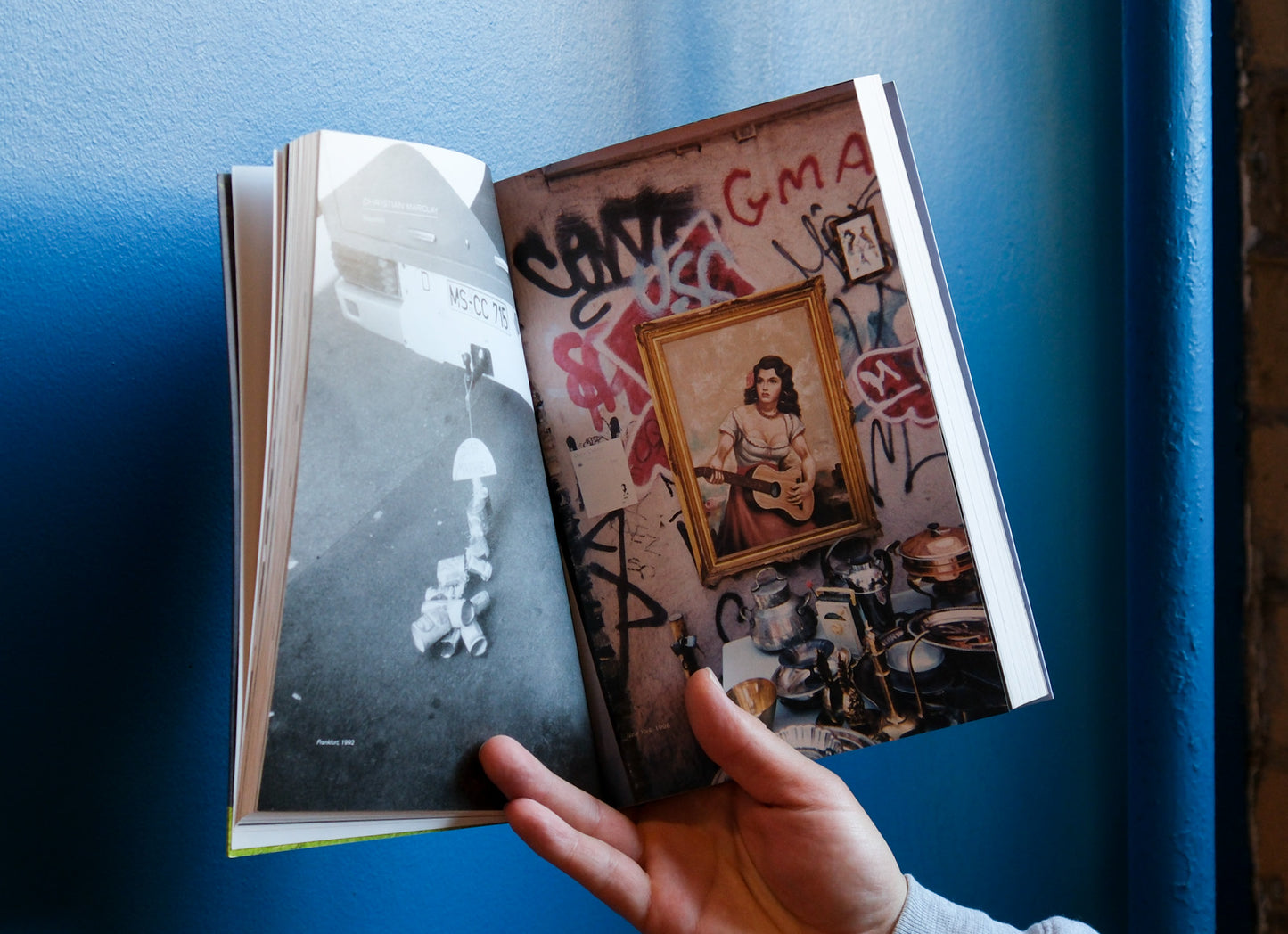 Book with a cover featuring a framed picture of a woman playing guitar, held against a blue wall.