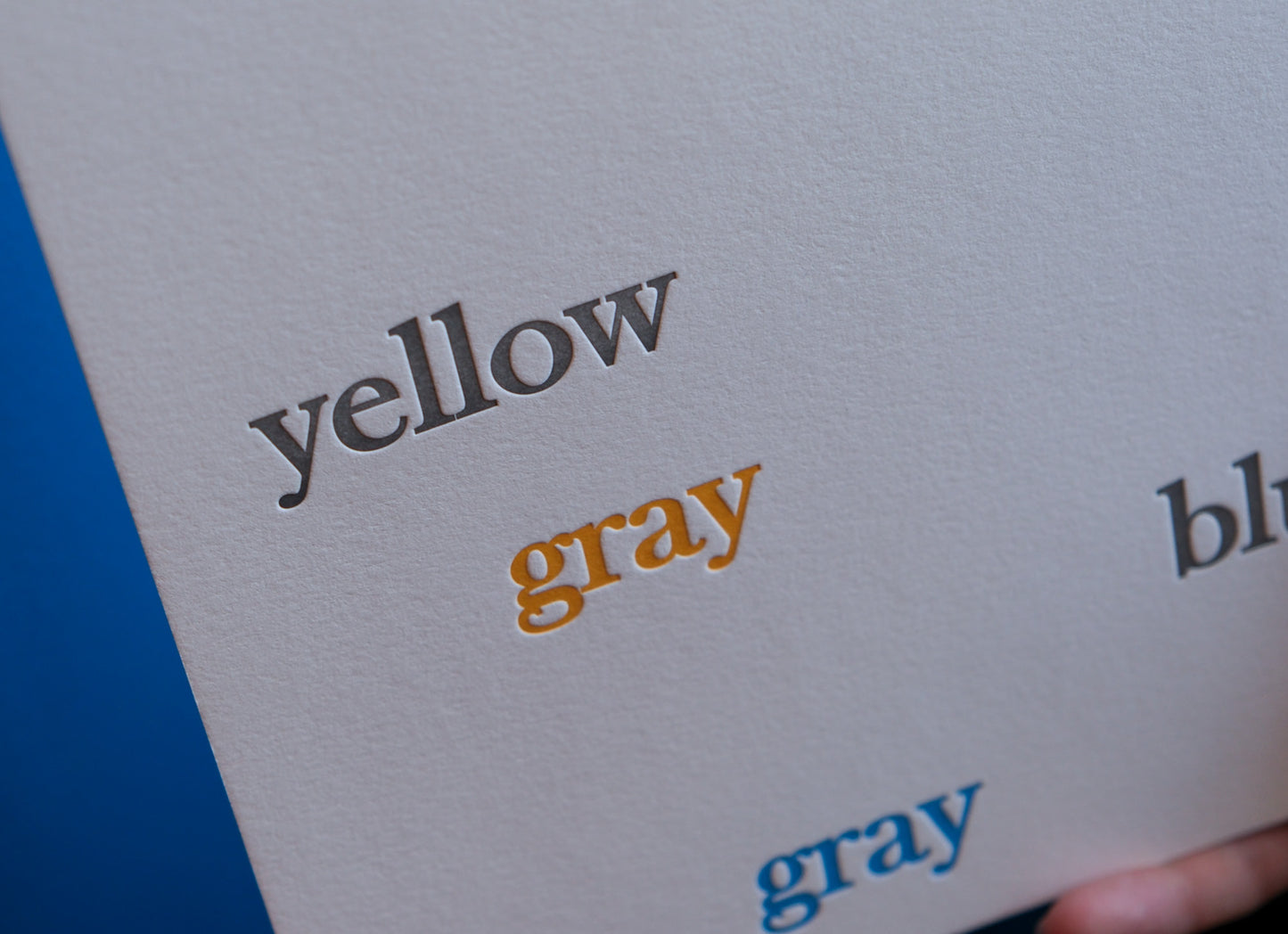 Close-up of a letterpress printed card with the words 'yellow', 'gray', and 'blue' text on a blue background.