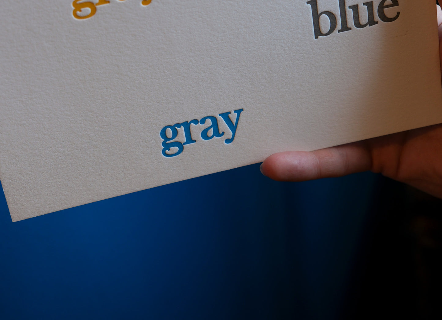 Hand holding a letterpress printed card with 'gray' and 'blue' text on a blue background