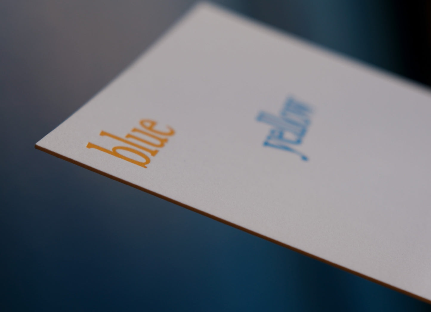 Close-up of a letterpress printed card with 'blue' printed on it against a dark background