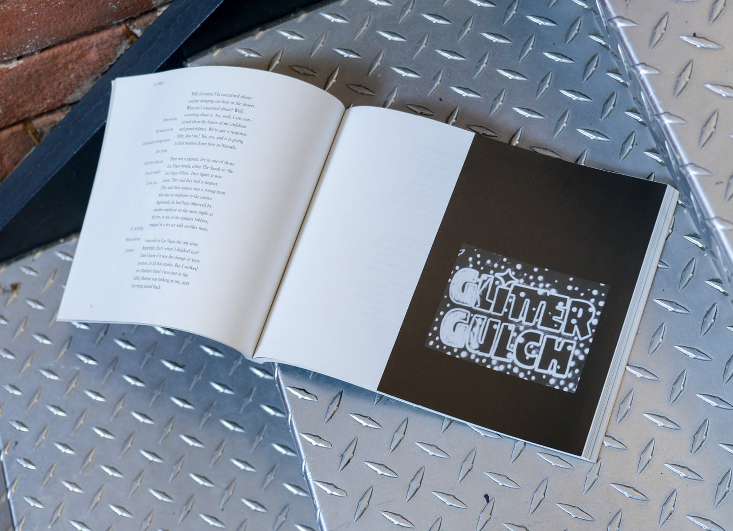 Open book with a black page featuring 'Glitter Gutch' design on a metallic surface.
