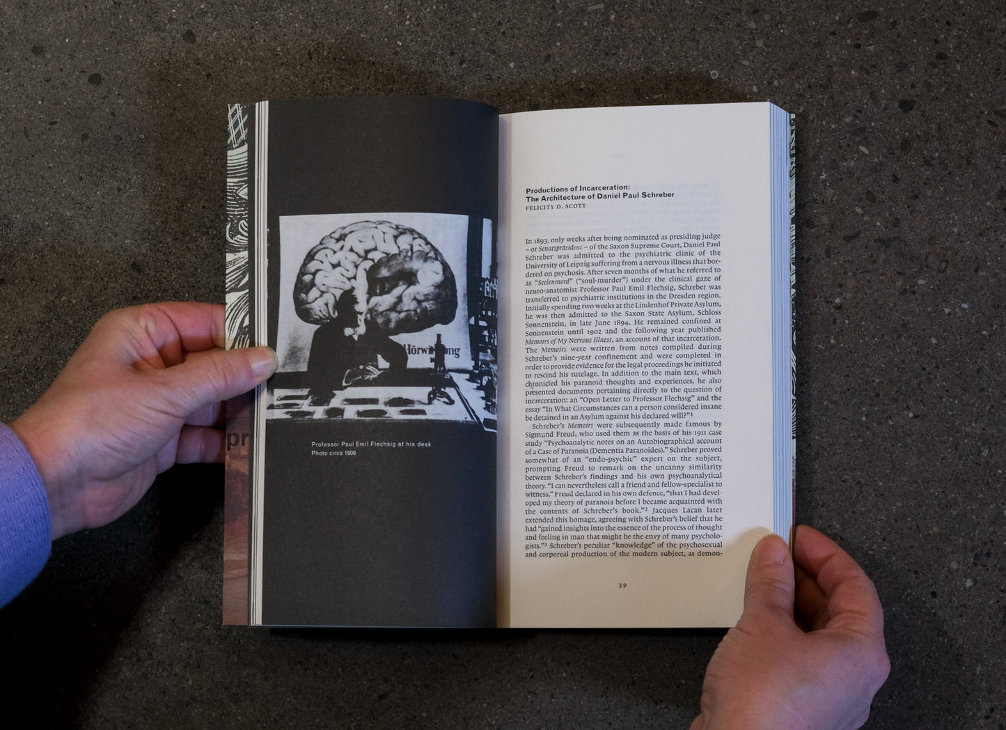 Open book held by a person with a black and white image of a brain on a dark textured surface