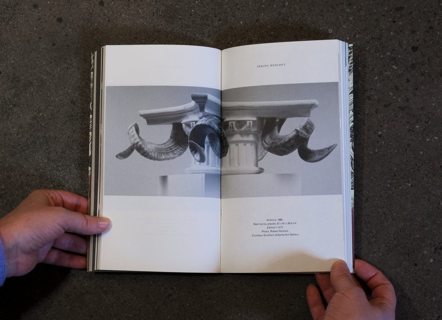 Open book held by a person with black and white images of architectural elements on a dark surface
