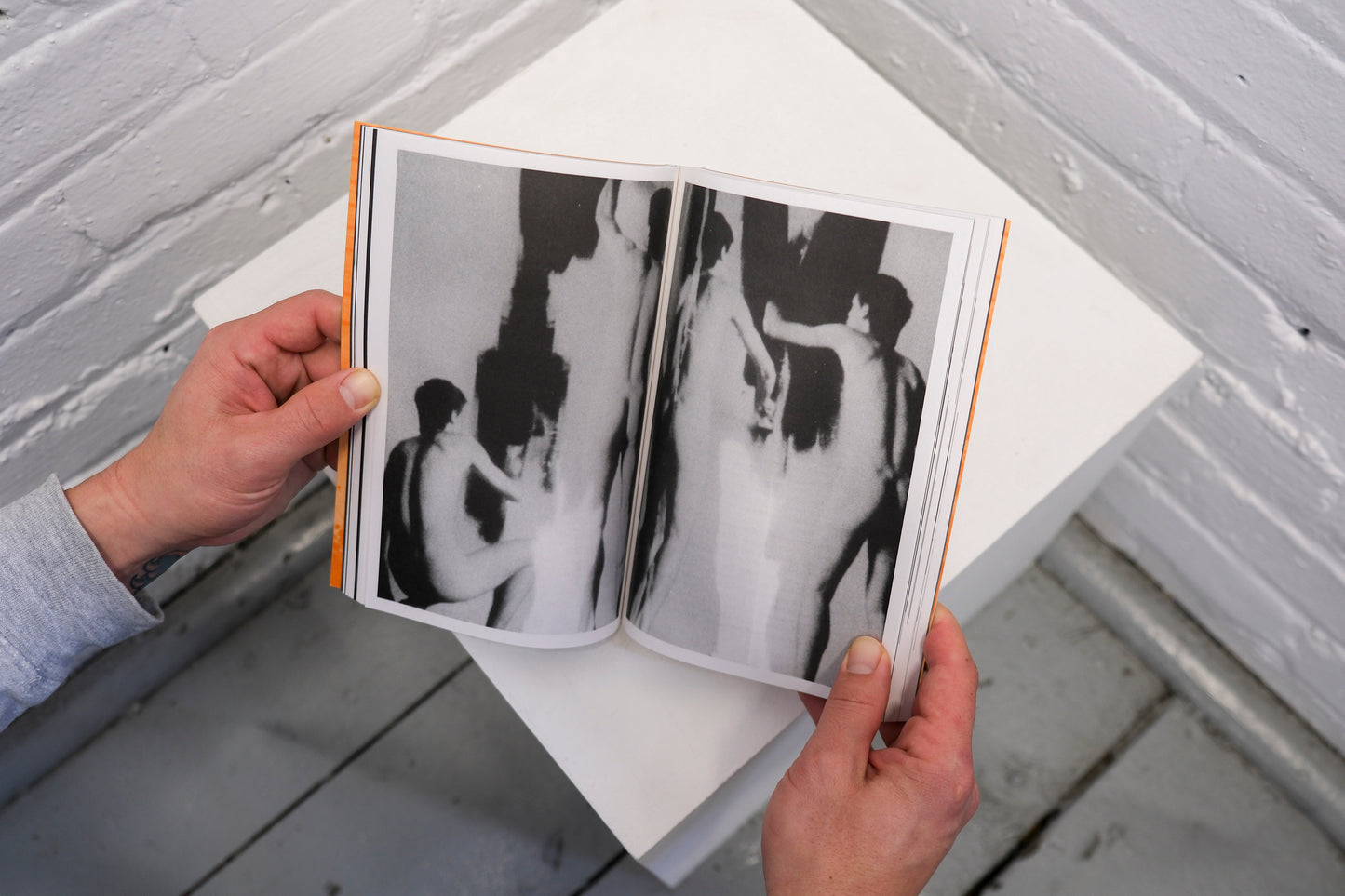 Person holding an open book with black and white abstract art pages against a light gray wall.