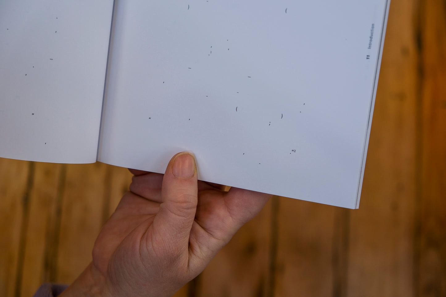 Hand holding a white book with black text against a wooden background