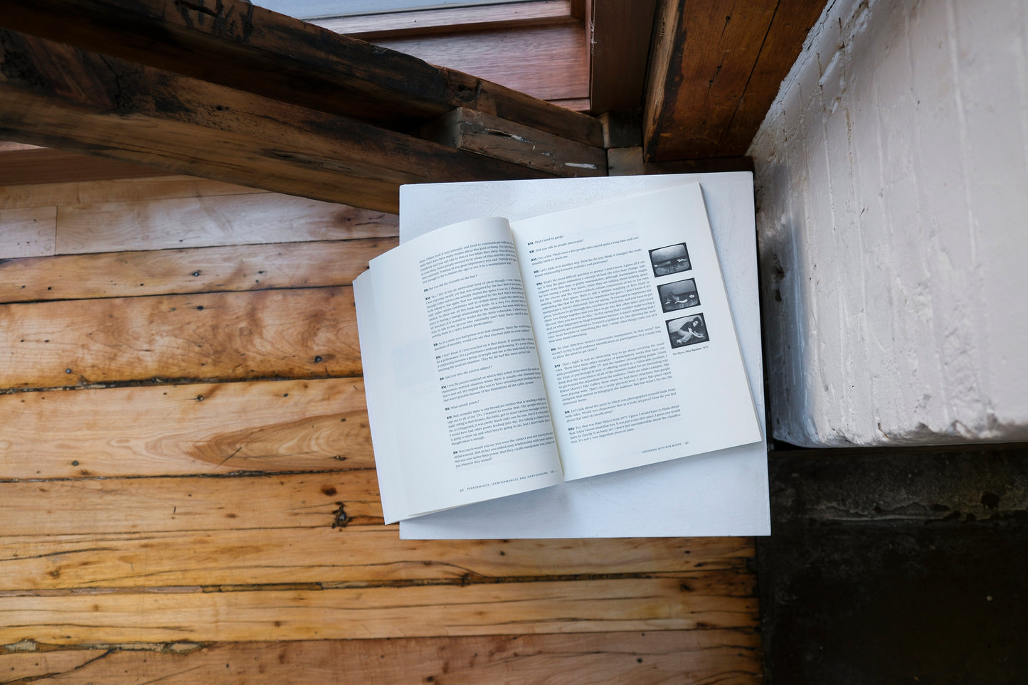 Open book on a plinth on a wooden surface with a brick wall in the background