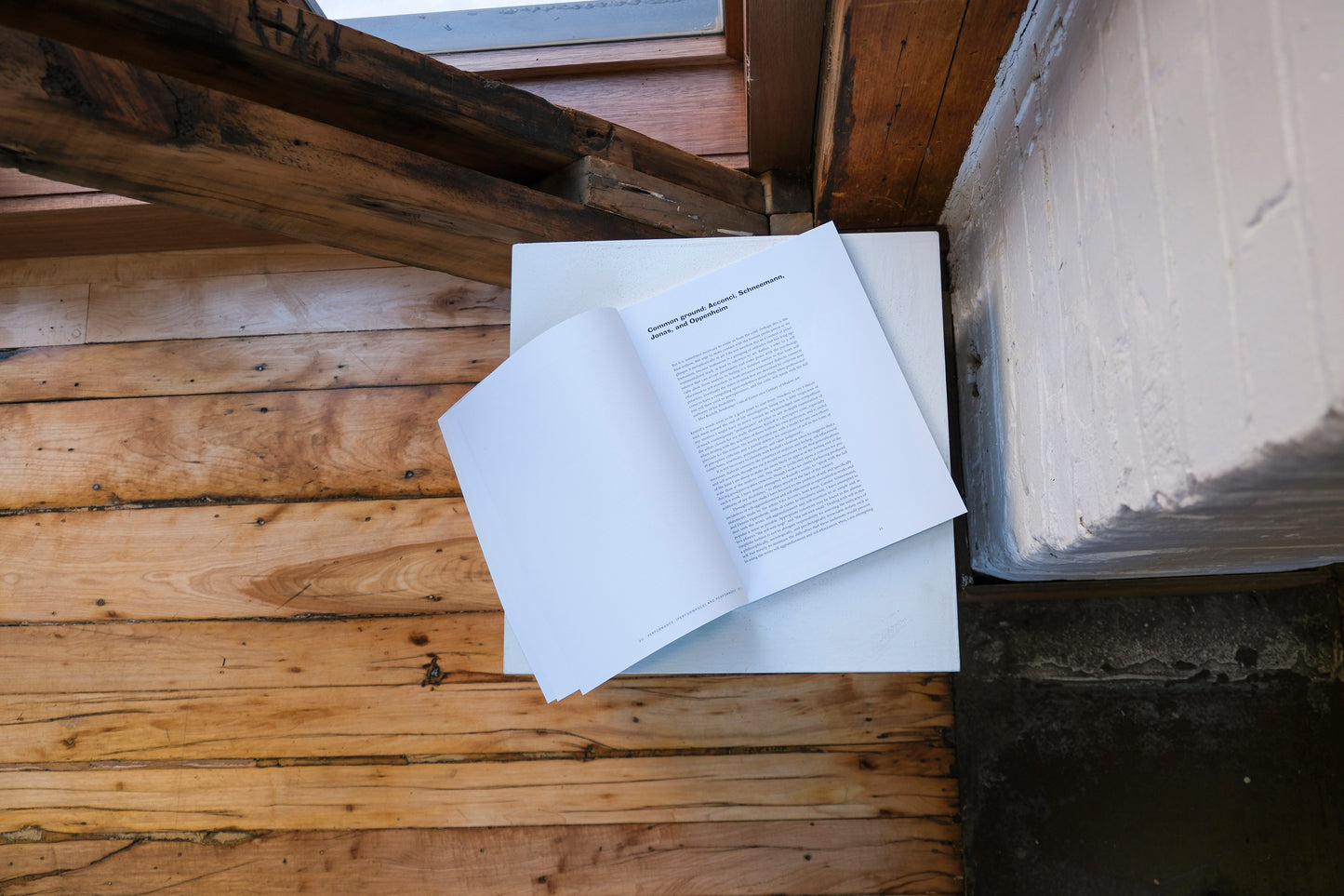 Open book on a plinth on a wooden surface with a brick wall in the background