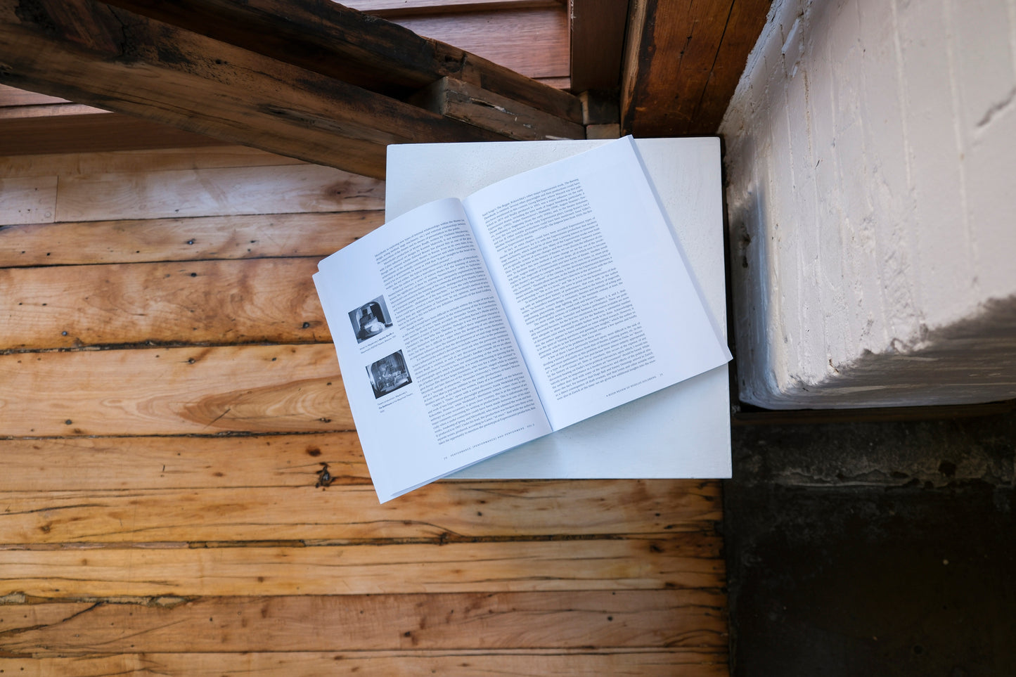 Open book on a plinth on a wooden surface with a brick wall in the background