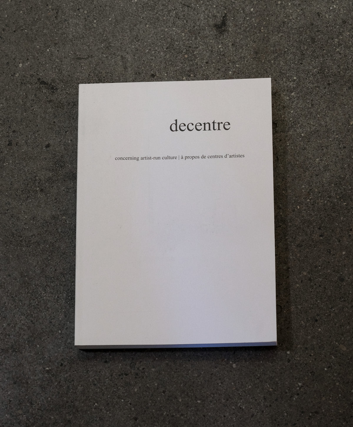 White book titled 'decentre' on a dark textured surface