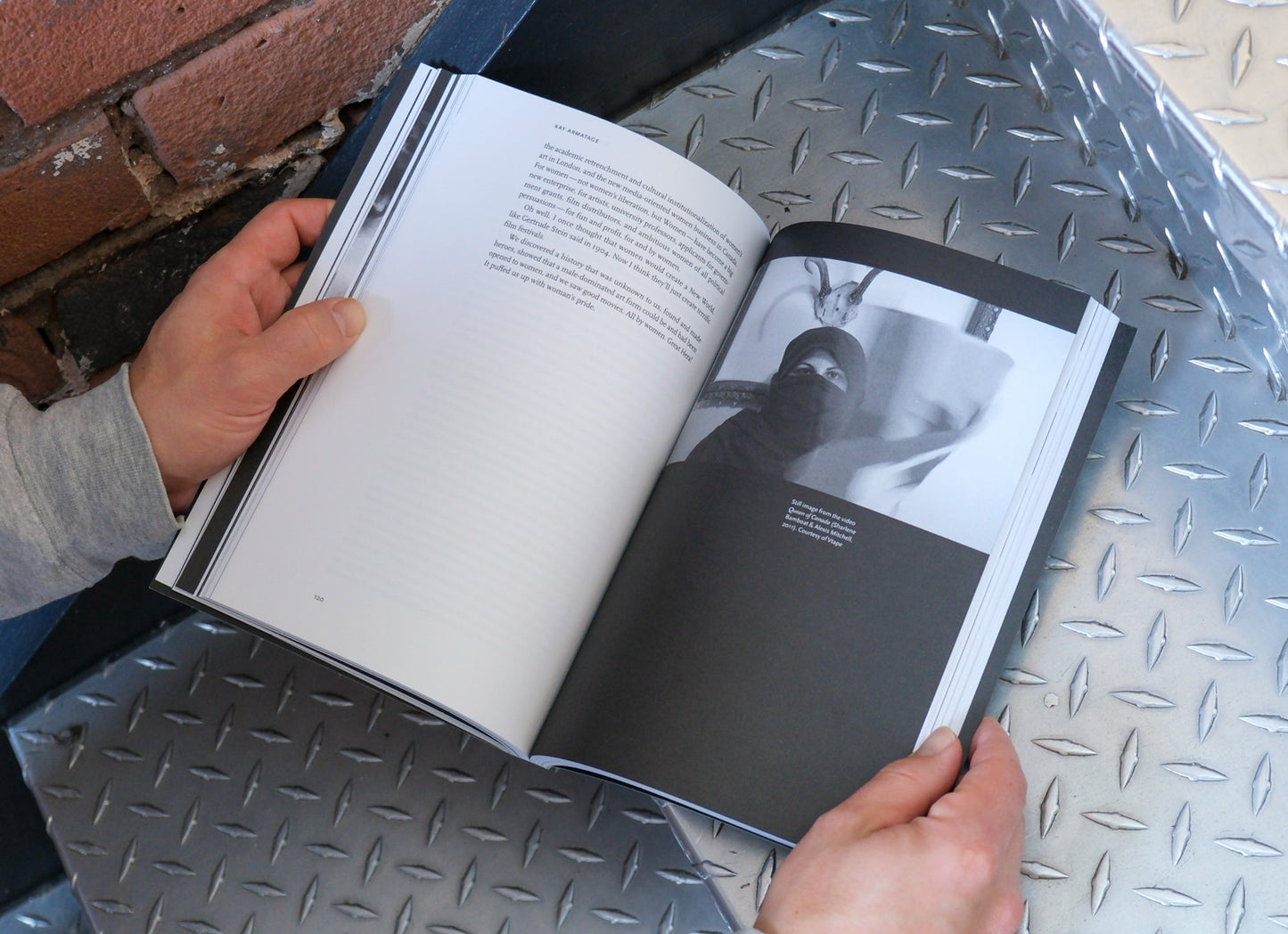 Person holding an open book with black and white images on a metal surface.
