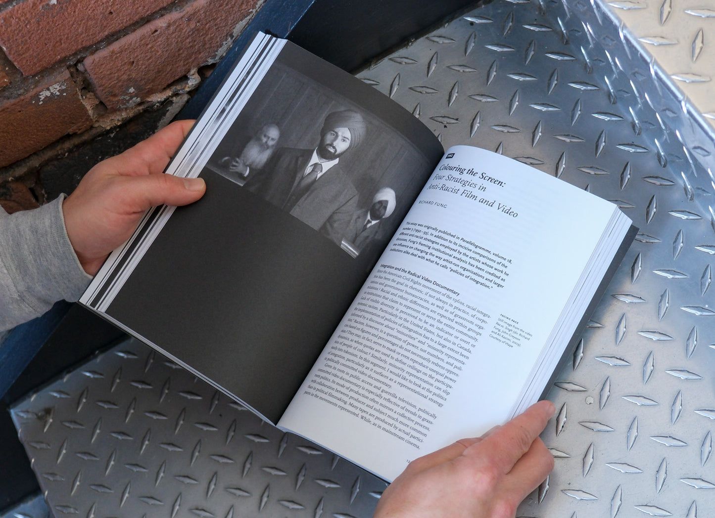 Person flipping through a book on a metal surface with a brick wall in the background