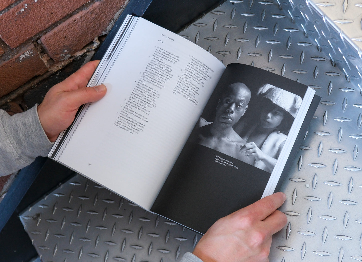 Person holding an open book with black and white photographs on a metal surface.