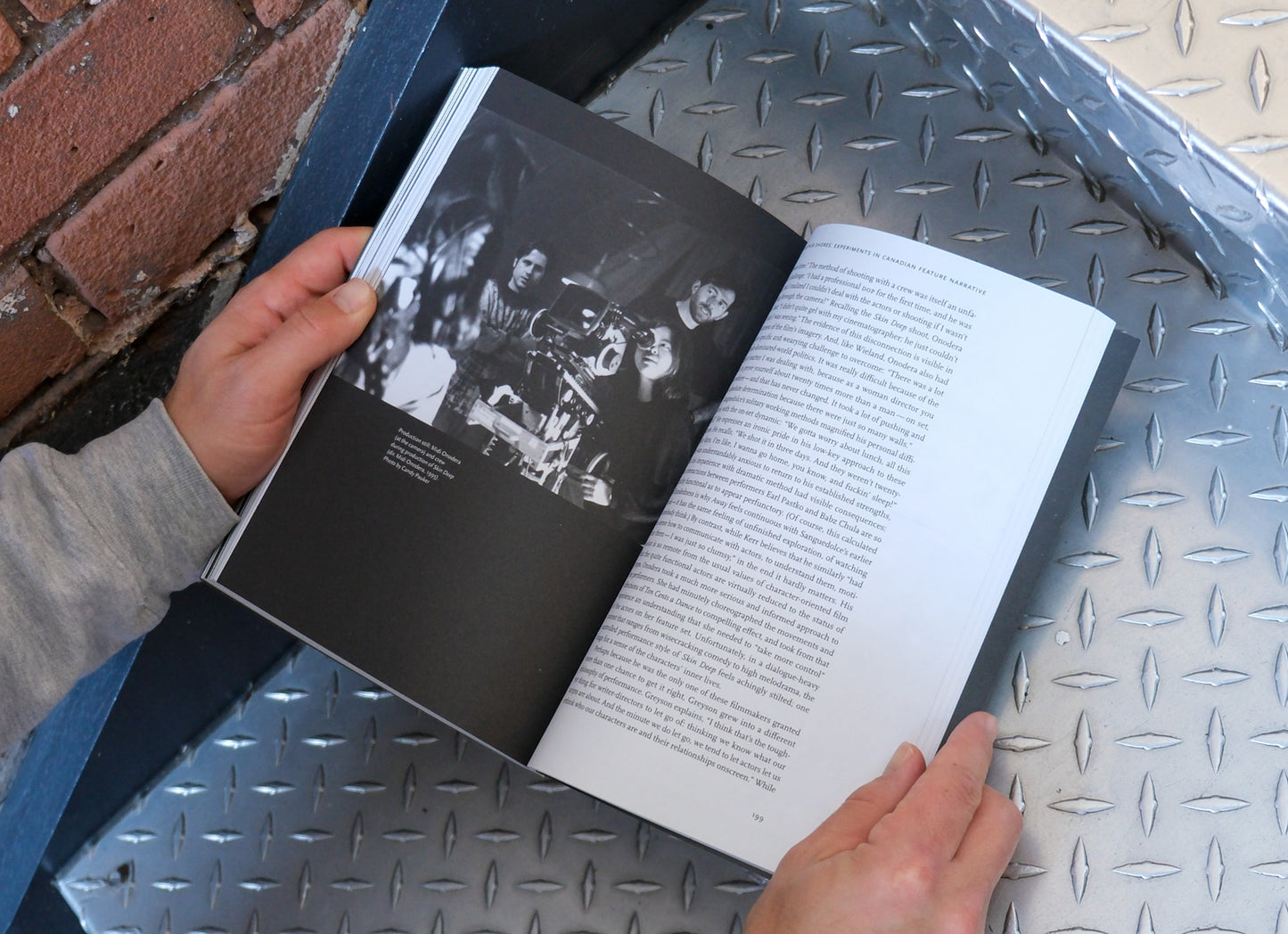 Person holding an open book with black and white images on a metallic surface.