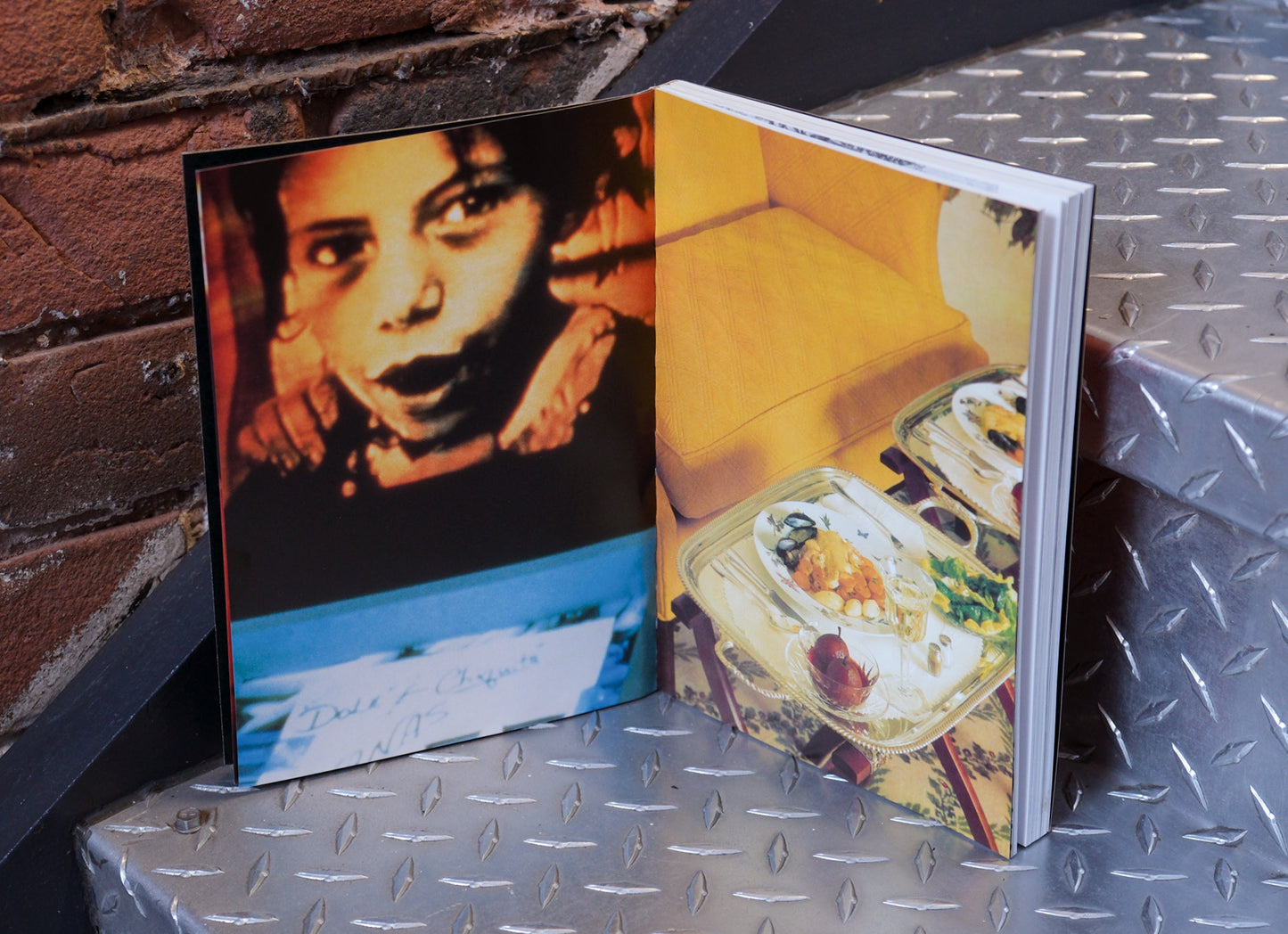 Open book with a photograph of a child on one page and a meal on the other, placed on a metallic surface.