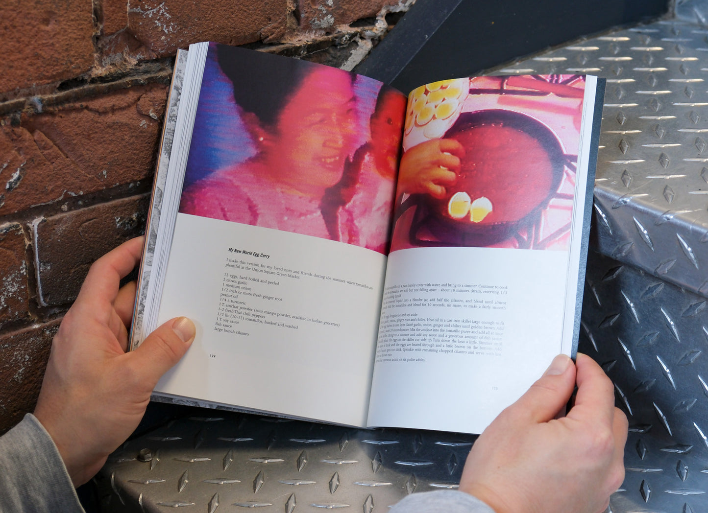 Person holding an open book with colorful images on a metal surface.