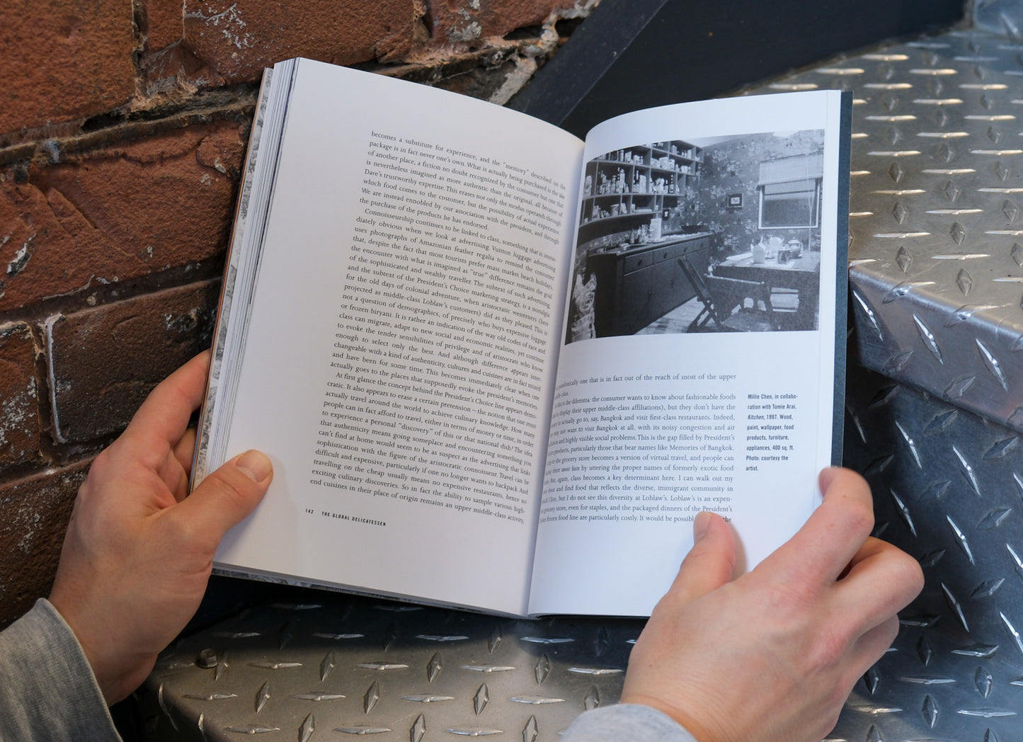Person holding an open book with text and a black and white photo against a brick wall.