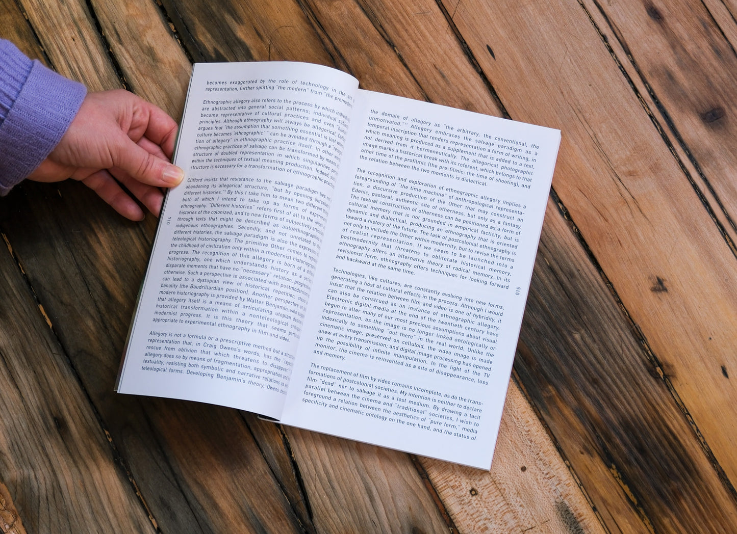 Open book on a wooden surface with a hand holding it