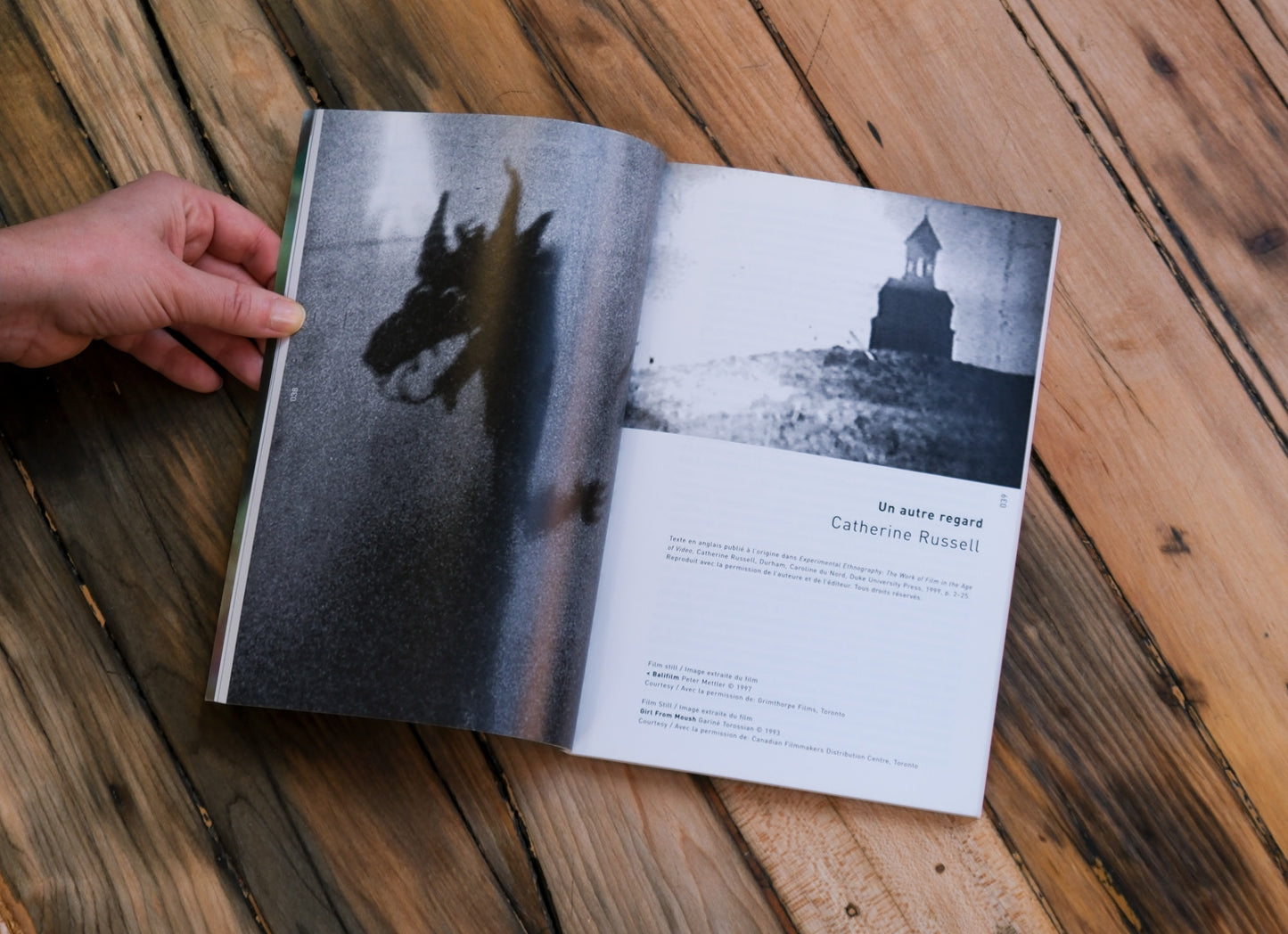 Open book on a wooden surface of black and white images and text with a hand holding it.