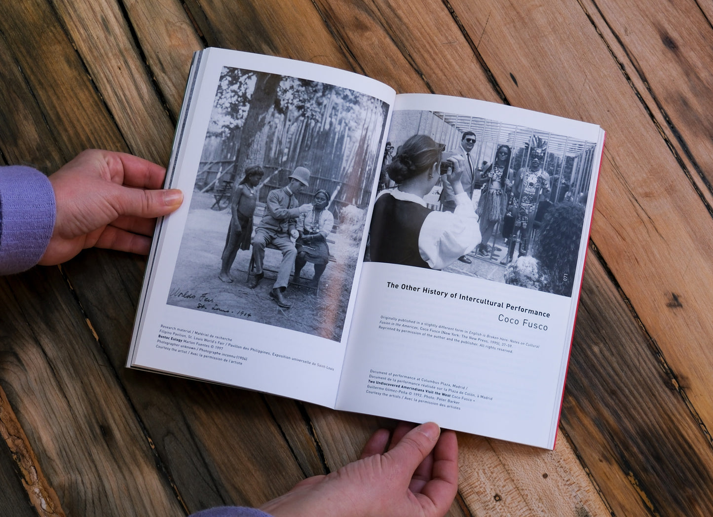 Open book on a wooden surface with black and white photos and text and hands holding it open.