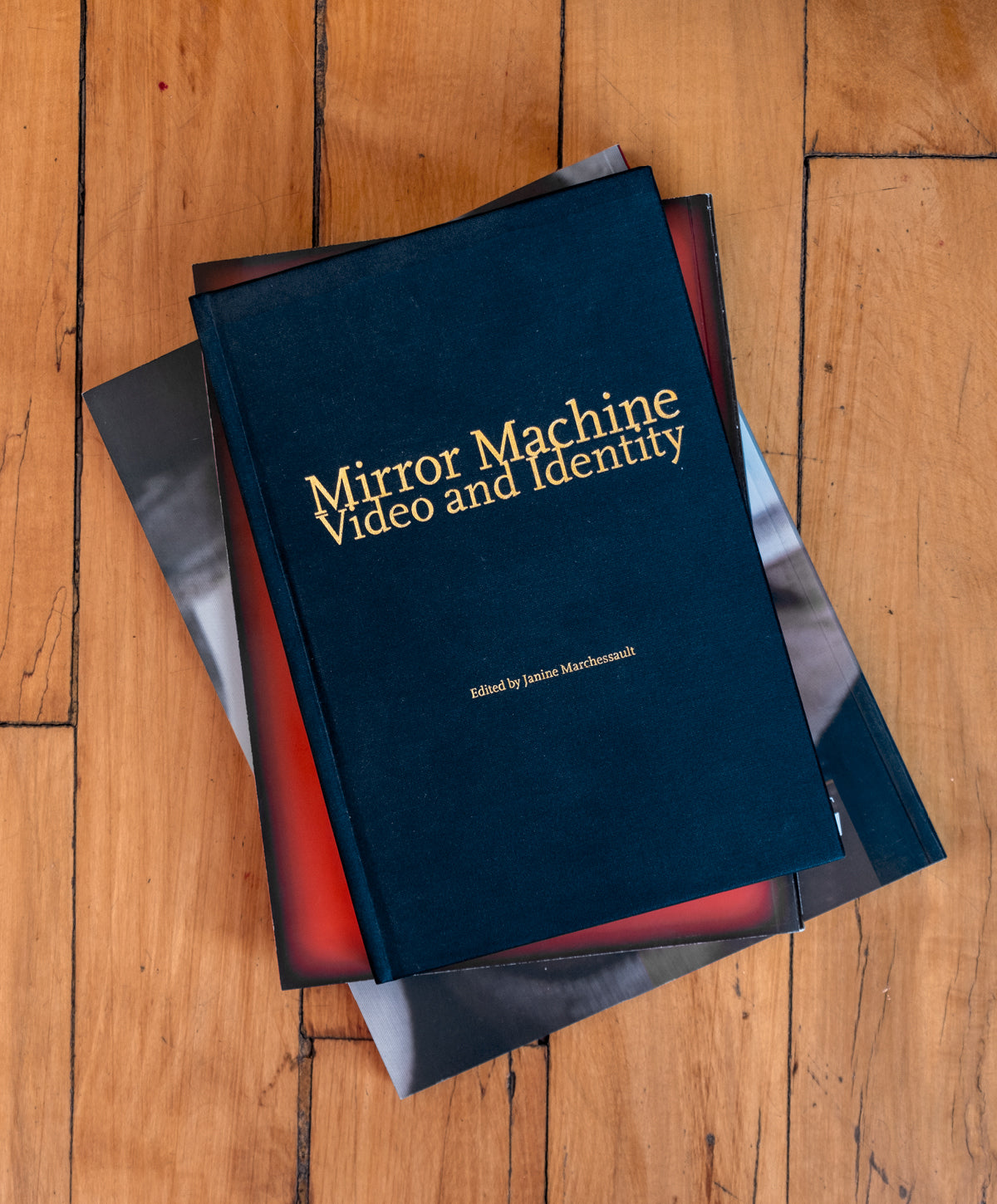 Hardcover version of Mirror Machine: Video and Identity cover on a stack of books on a wood floor