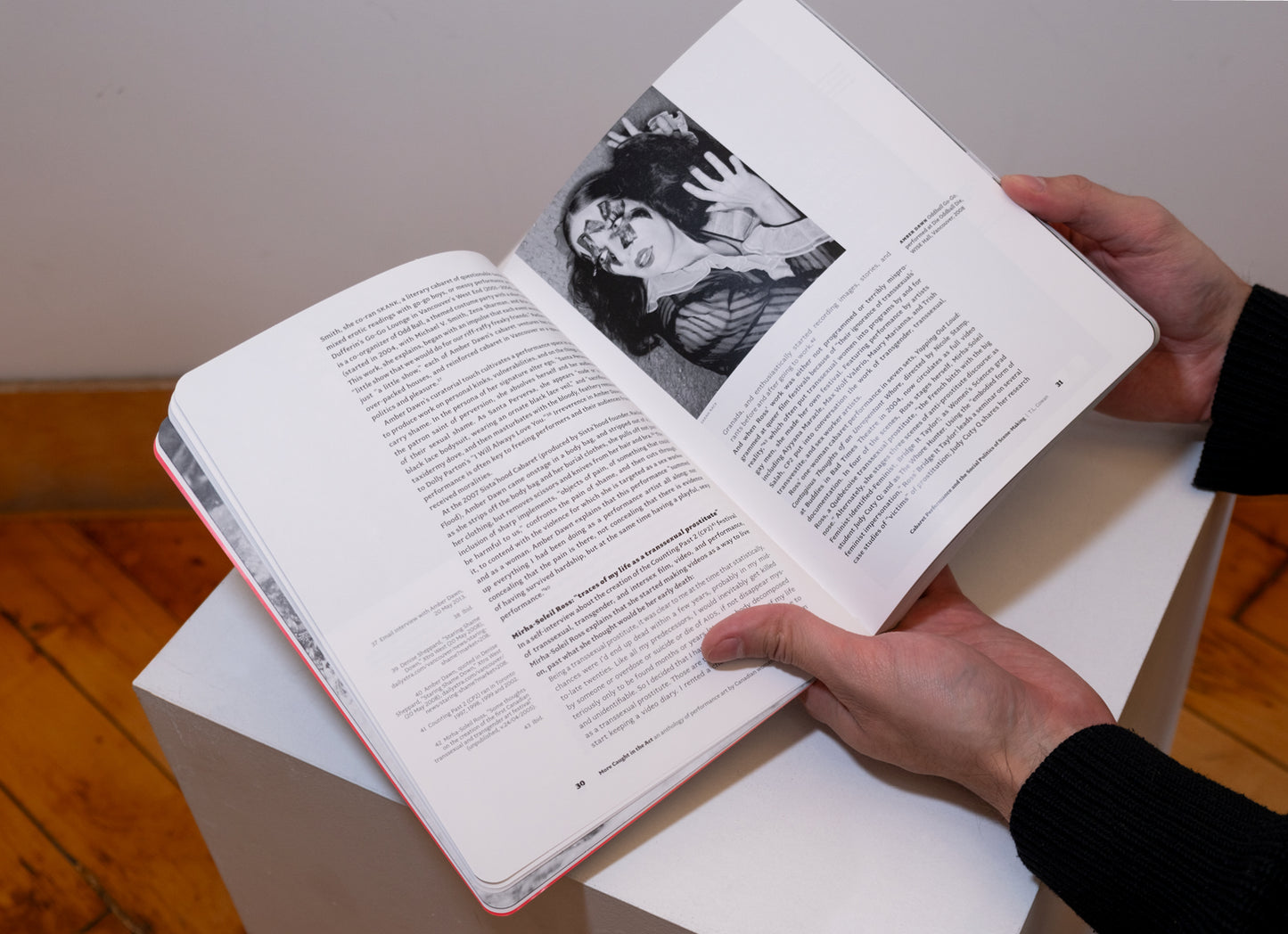 Hands holding More Caught in the Act: An Anthology of Performance Art by Canadian Women opened on plinth to show pages