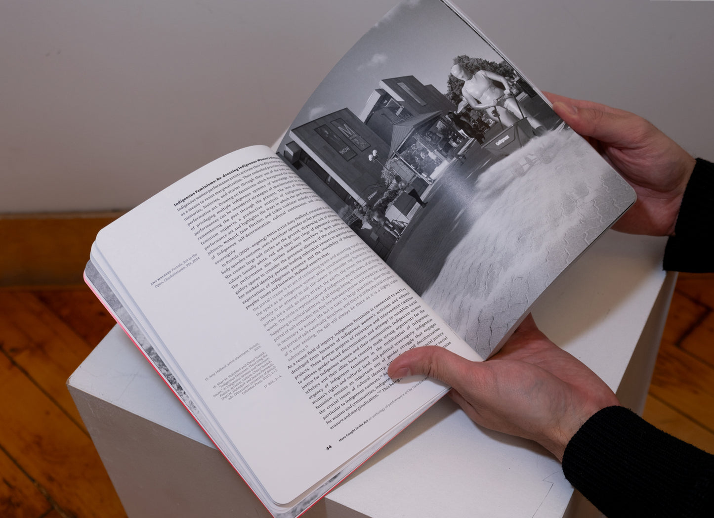 Hands holding More Caught in the Act: An Anthology of Performance Art by Canadian Women opened on plinth to show pages