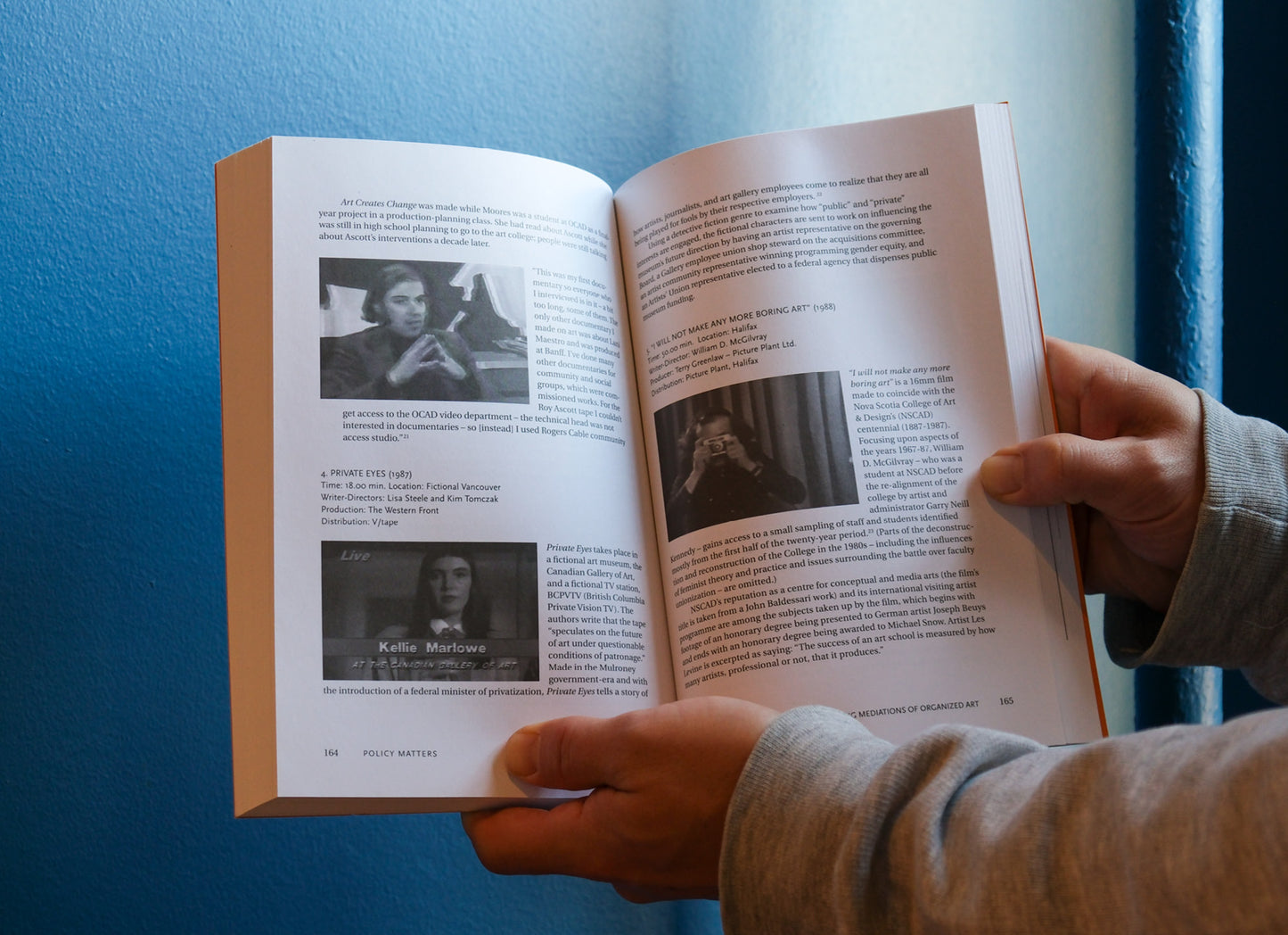 Person holding an open book with text and images against a blue wall.