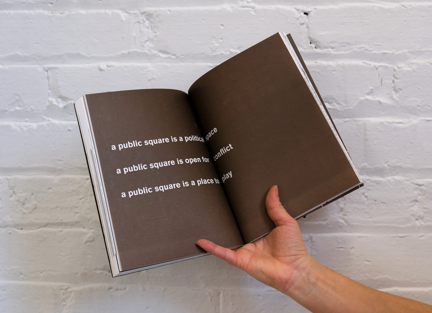Open book with text held against a white brick wall