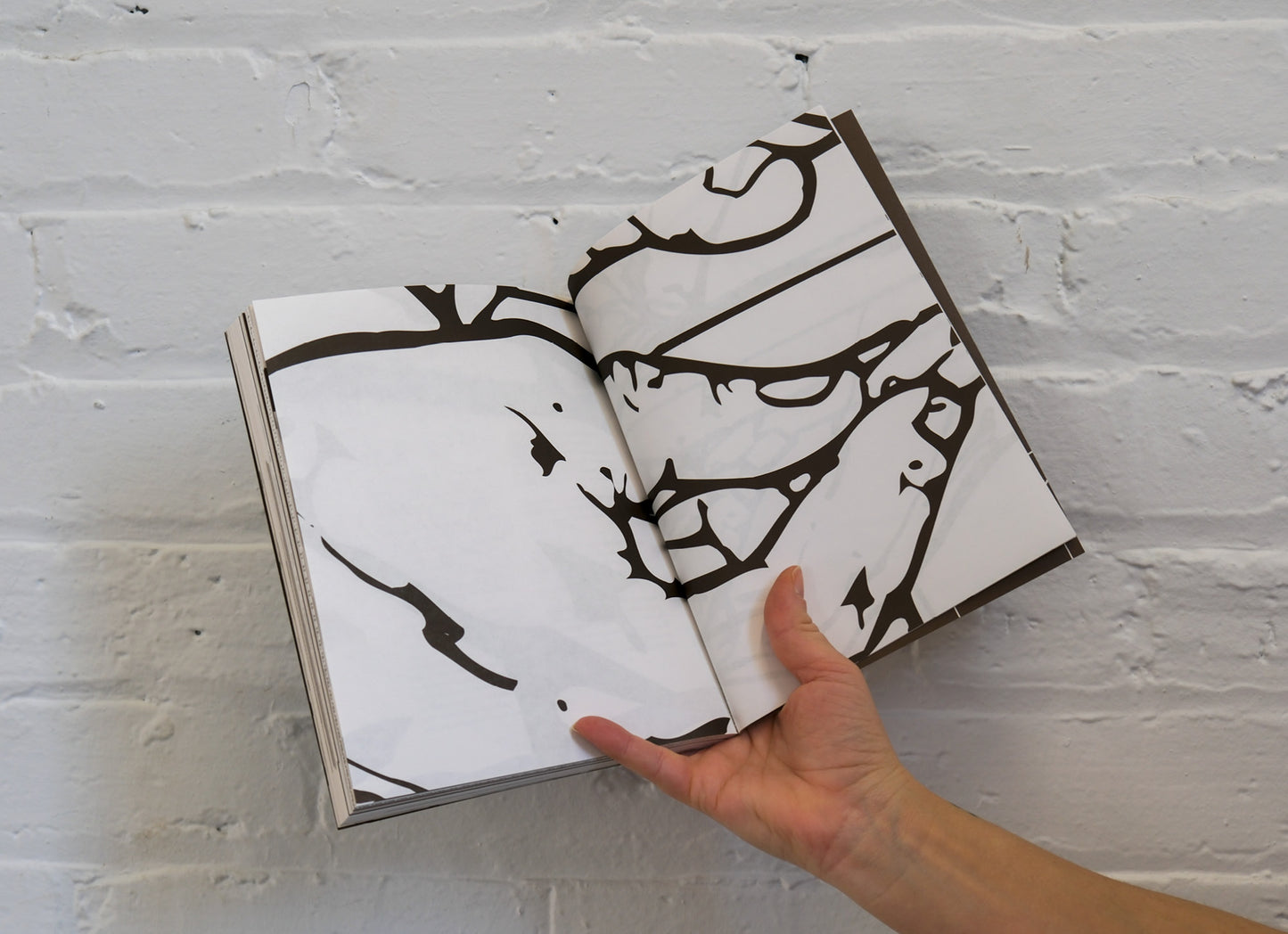 Open book with black and white abstract art against a white brick wall.
