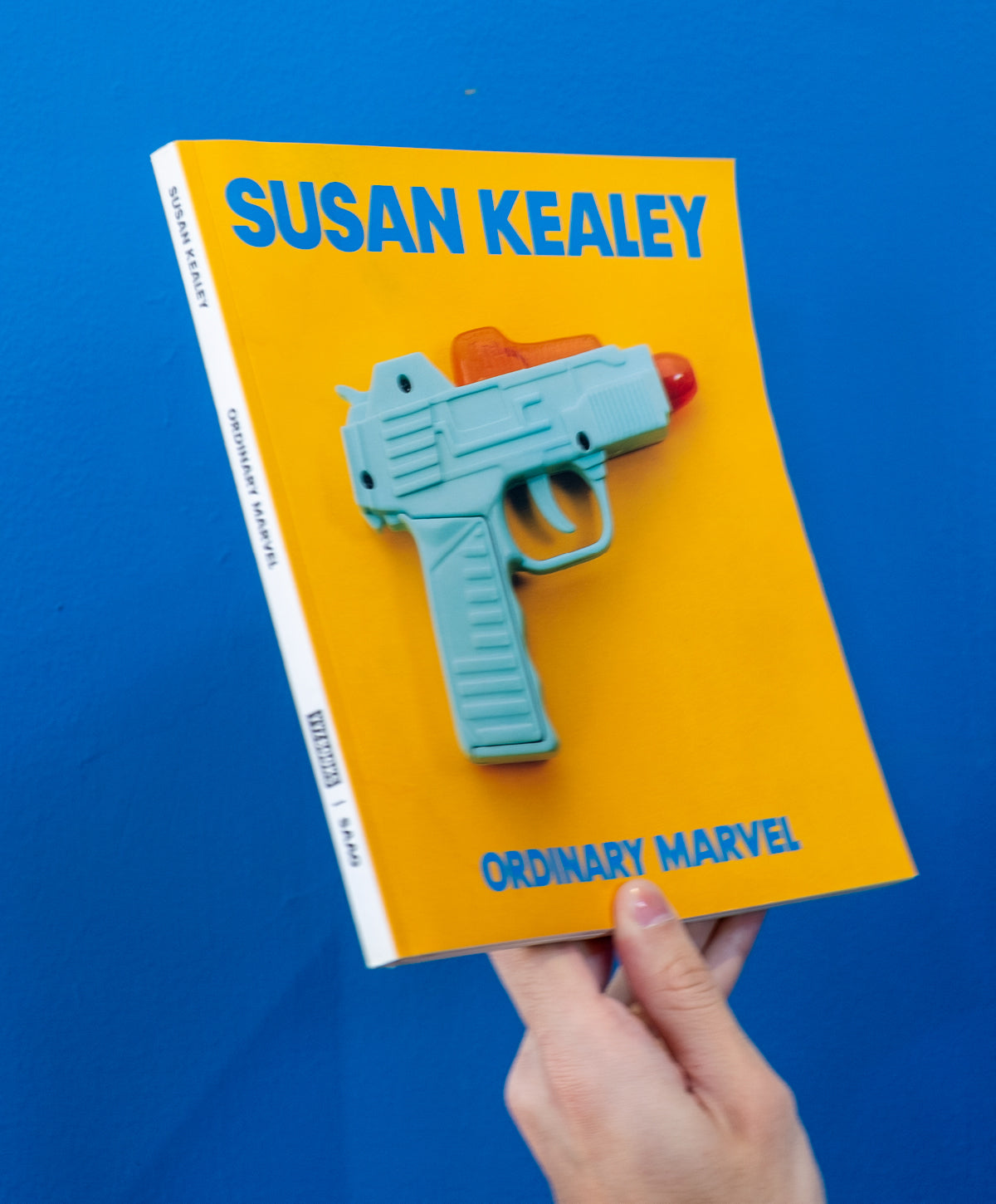 Hand holding Susan Kealey: Ordinary Marvel cover against a blue wall