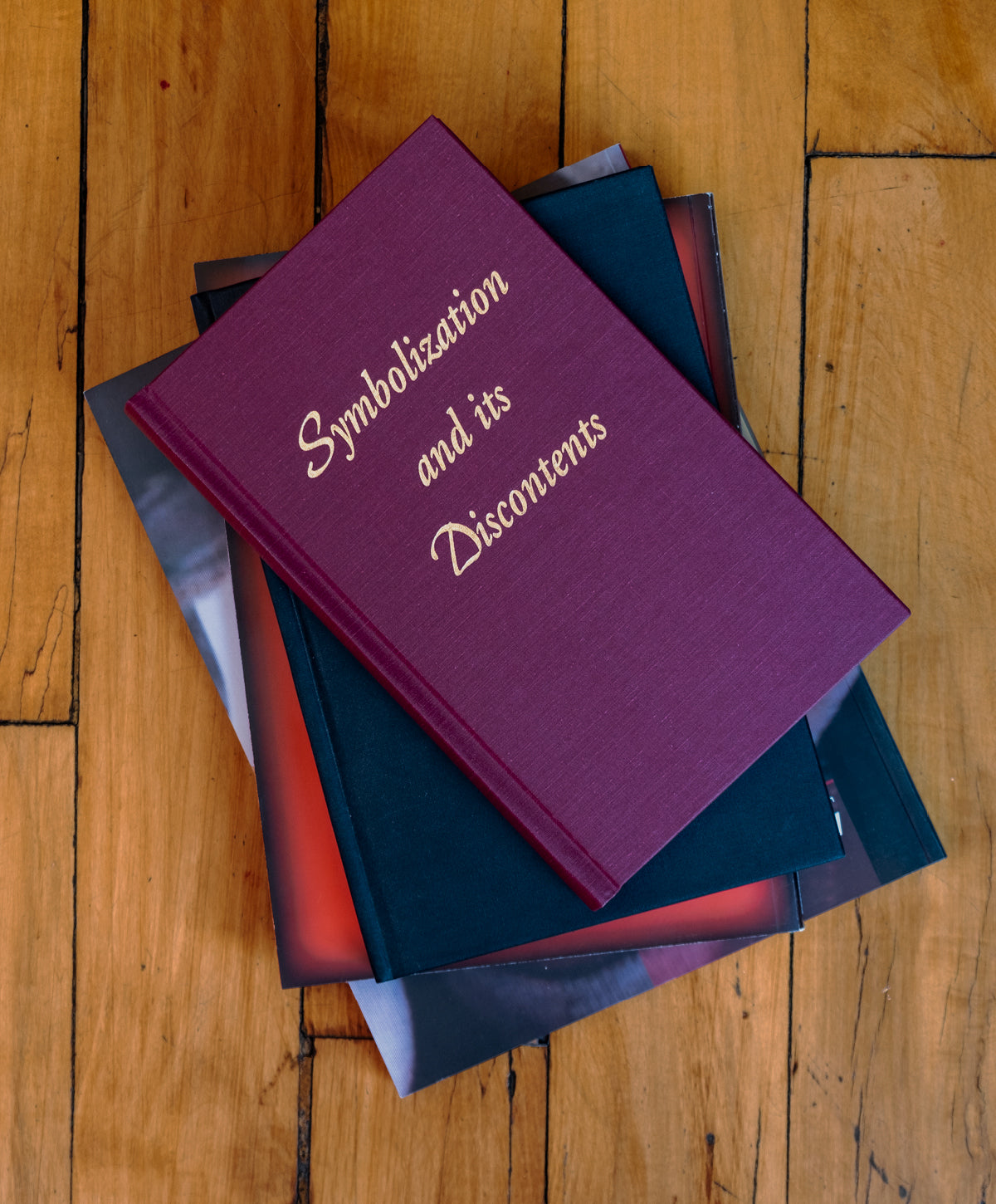 Maroon hardcover Symbolization and Its Discontents with gold type, laying on a stack of books