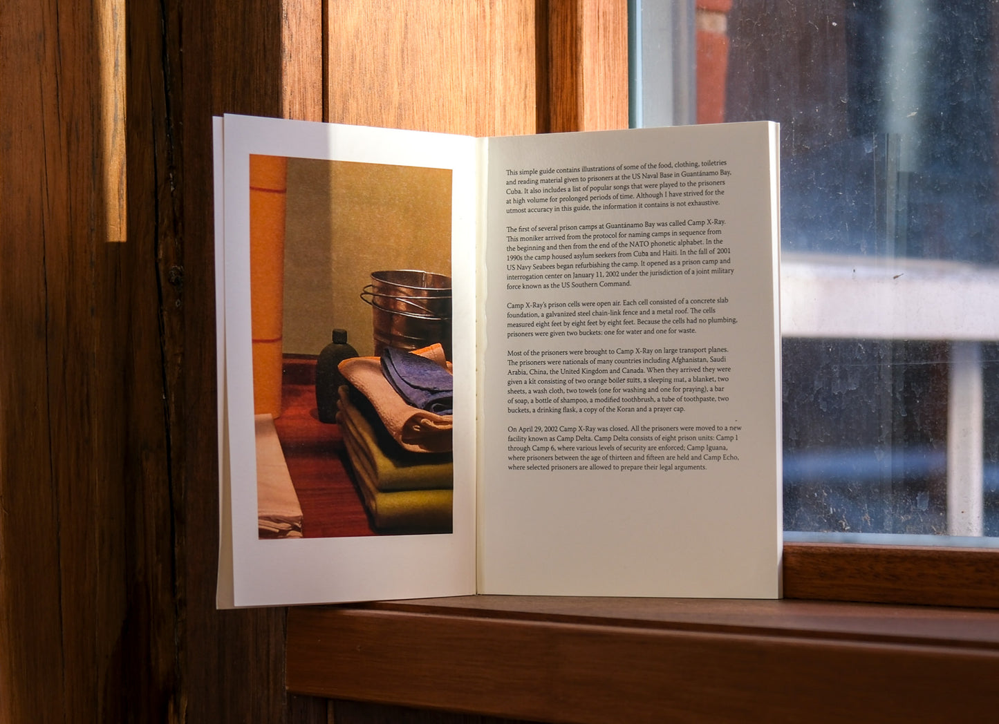 Open book with a photograph and text on a wooden surface near a window.